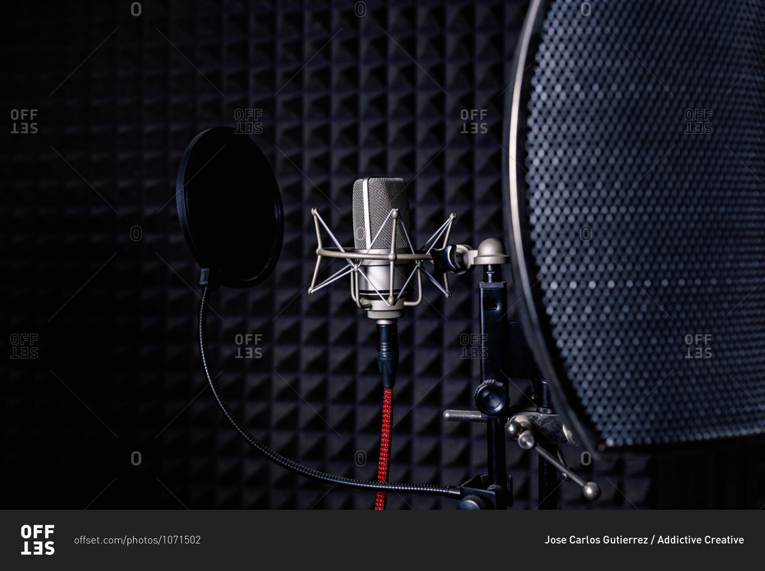 Contemporary metal microphone with wire placed on background of soundproof foam with pyramid shaped pattern in dark music recording studio