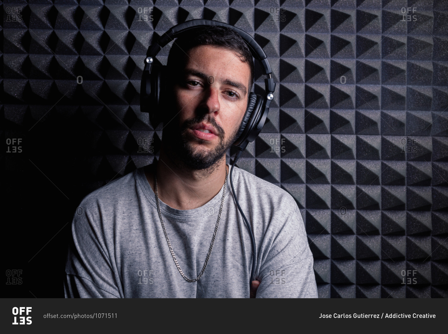 Stylish male singer wearing headphones standing in recording studio on background of soundproof acoustic panel and looking at camera
