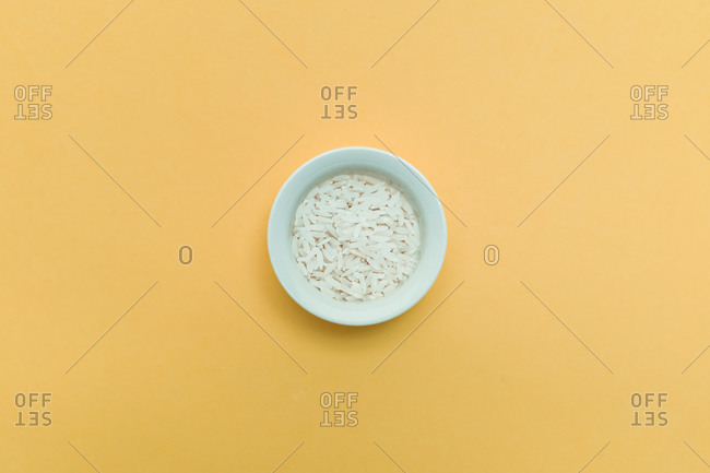 Top view of ceramic bowl of rice placed on yellow background in studio