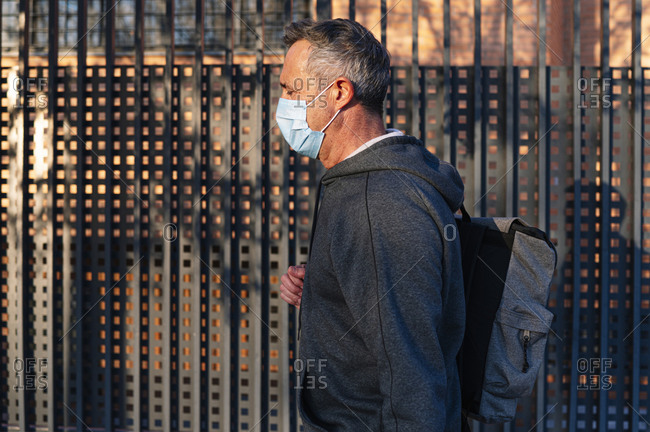 Senior retired man with face mask and sportswear walking down the street