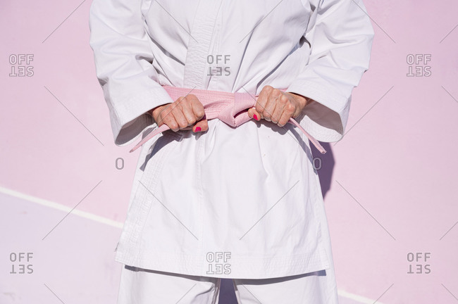Cropped unrecognizable determined mature woman in pink head cover and belt fighting karate in cancer battle concept in the street on pink wall