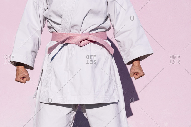 Cropped unrecognizable determined mature woman in pink head cover and belt fighting karate in cancer battle concept in the street on pink wall