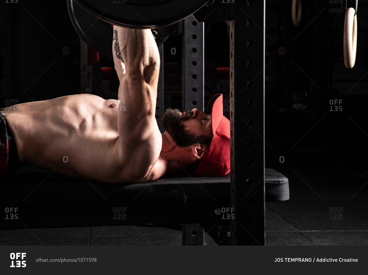 Side view of strong focused male athlete lying on bench press and doing exercises with heavy barbell during workout in gym
