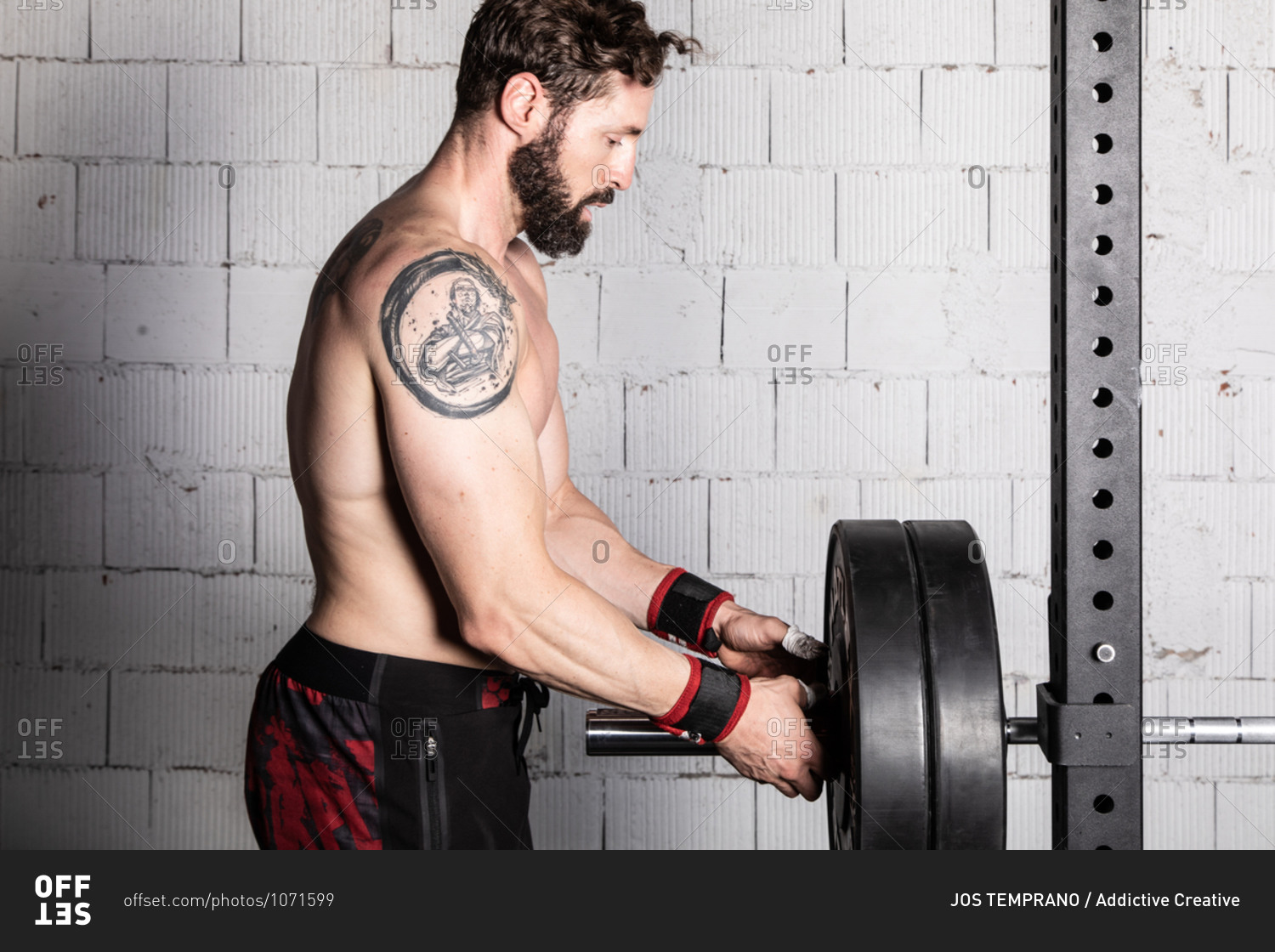 Side view of shirtless muscular male athlete preparing heavy barbell for weightlifting workout in sports club