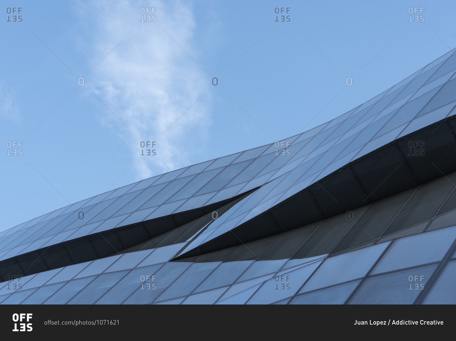 From below of futuristic building with wave shaped exterior made of glass panels located against blue sky in city center