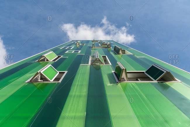 From below contemporary building with vivid green facade and opened windows on blue sky
