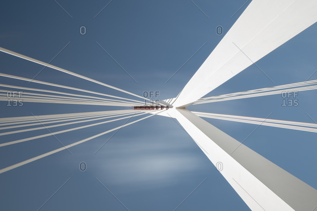 From below of white contemporary suspension bridge with high column connecting many cables together against blue sky