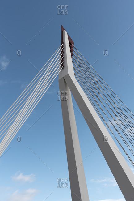 From below of white contemporary suspension bridge with high column connecting many cables together against blue sky