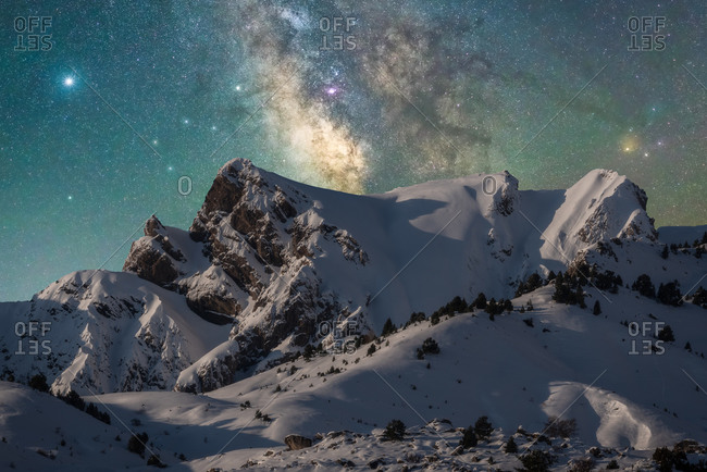 Spectacular view of high rough ridge covered with snow under colorful starry sky during milky way phenomenon