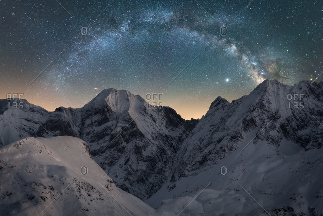 Spectacular view of high rough ridge covered with snow under colorful starry sky during milky way phenomenon