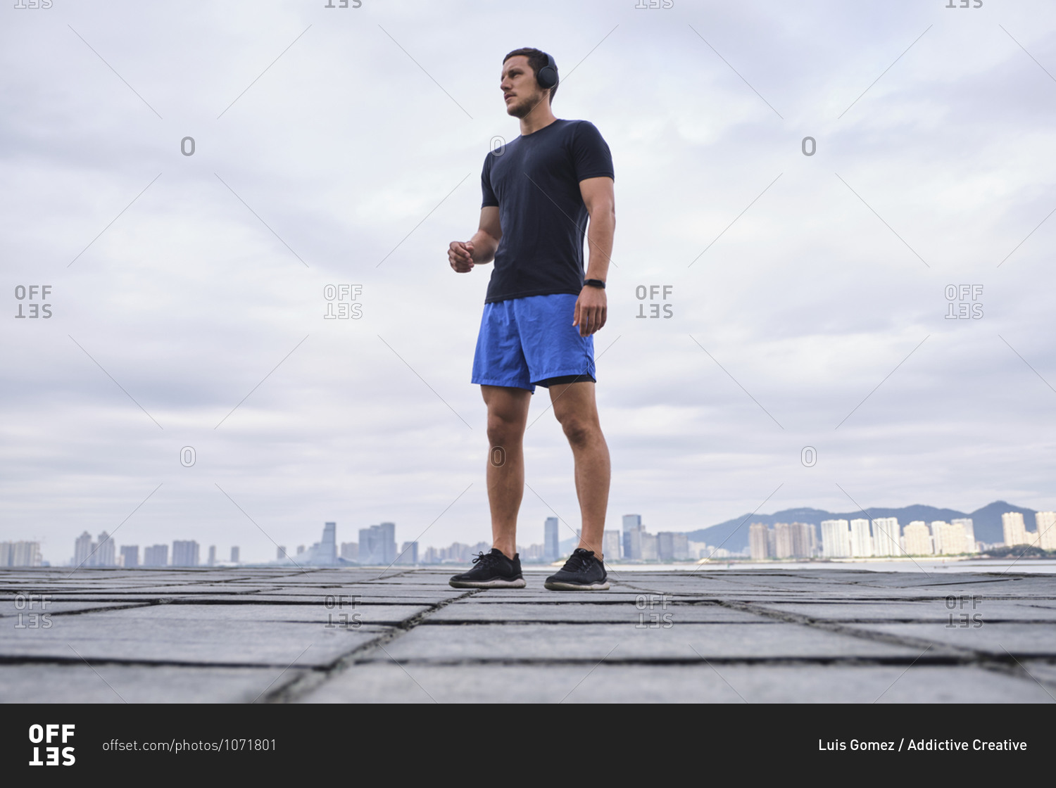 Ground level of determined male athlete in wireless headphones listening to music during workout while standing and looking away