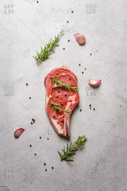 Top view uncooked t bone beef steak garnished with black pepper and rosemary sprigs placed on table in kitchen