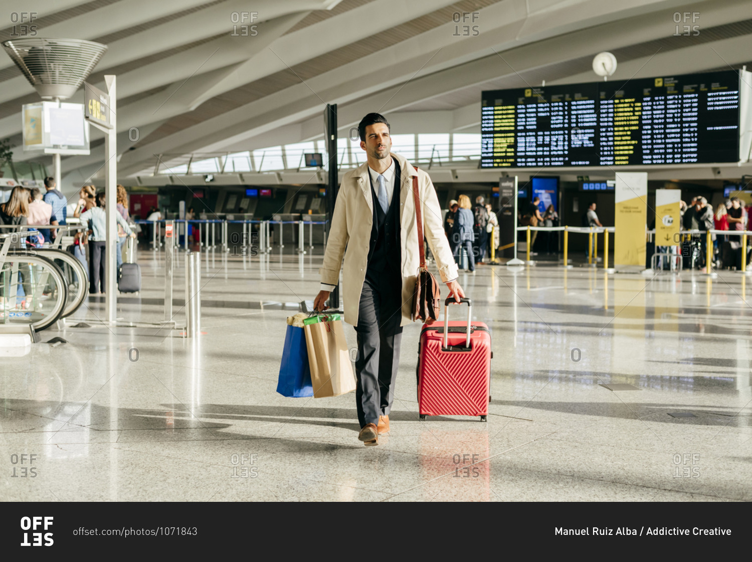 Man with dark hair in stylish clothes walking with suitcase in terminal of airport