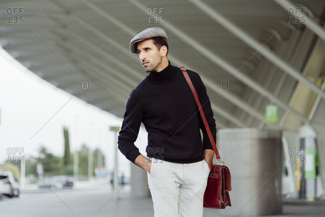 Front view of man with beard in trendy clothes walking on street near asphalt road with parked cars at daytime