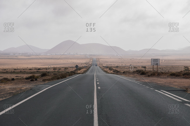 Endless asphalt road going through dry savanna in mountainous terrain on overcast day