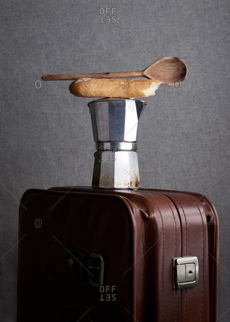 Simple composition of coffee maker with wooden old spoon and bread stick placed on leather suitcase