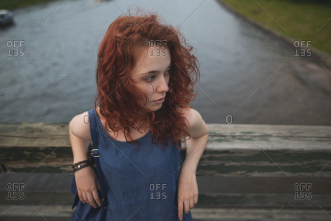 From above of young red haired female traveler in casual outfit with backpack resting near channel while exploring old architecture of Saint Petersburg in Russia during summer holidays