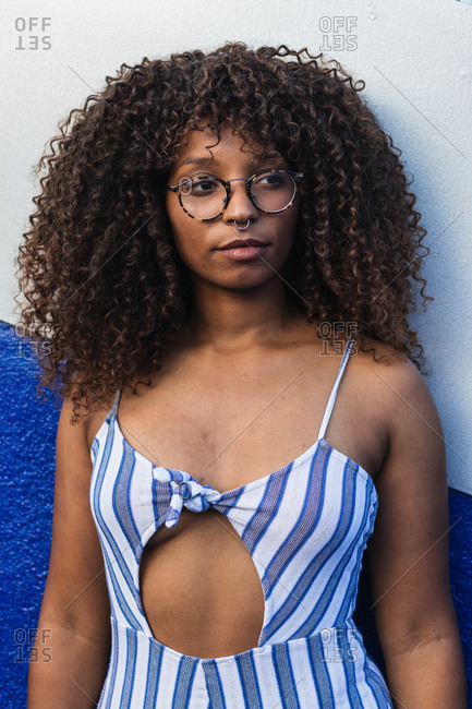 Young black woman with glasses and curly hair while standing near vivid wall on city street