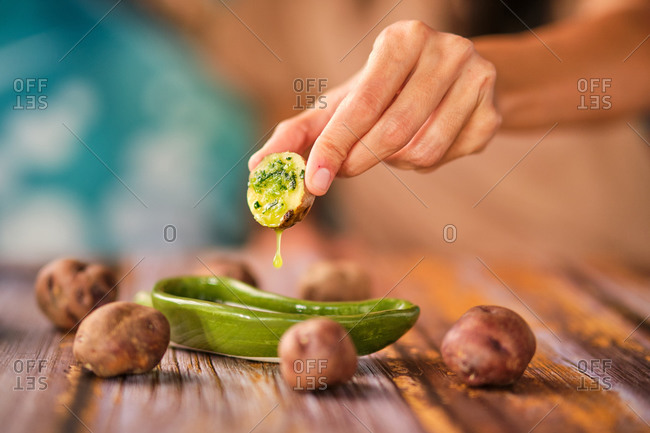 Crop unrecognizable person dipping yummy cooked potato in lemon salsa in decorative plate on wooden table