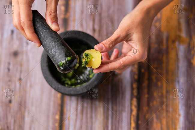 Overhead view of crop unrecognizable chef preparing sauce with fresh lemon and herb in mortar with pestle
