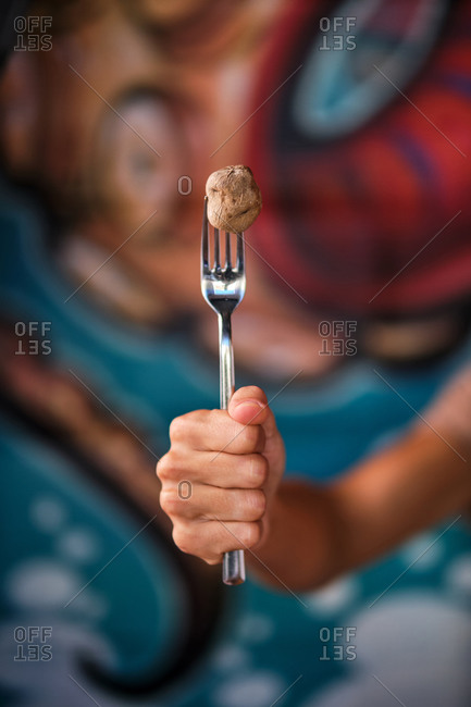 Crop anonymous person demonstrating shiny fork with small potato with wrinkled peel on blurred background