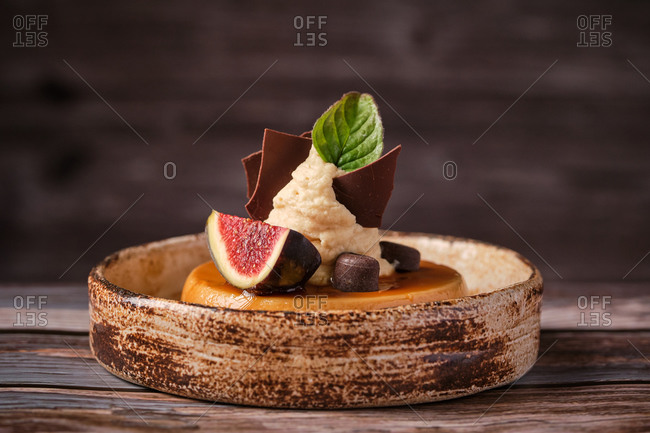 Tasty caramel cheesecake with fig and green basil in plate with spoon on wooden table in cafe