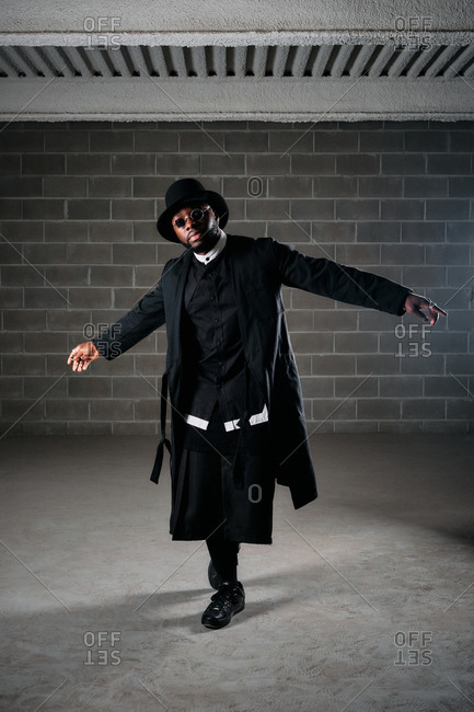 Low angle of African American male hip hop dancer in black apparel rehearsing in underground garage and showing choreography movements