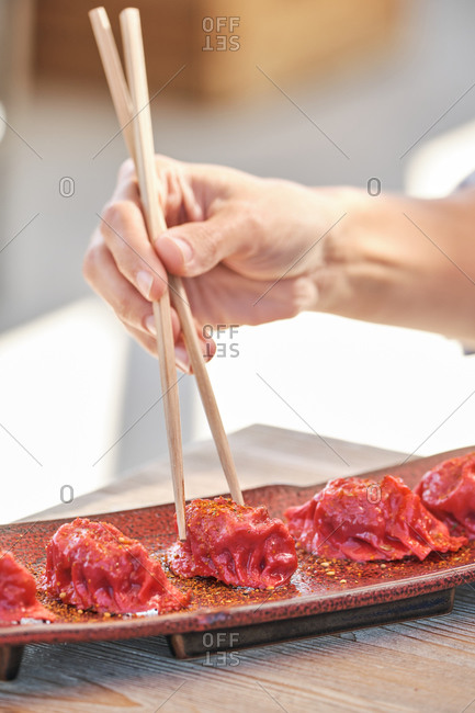 Cropped unrecognizable person hands holding chopstick eating delicious tuna sushi garnished with chili threads served on table in Asian restaurant