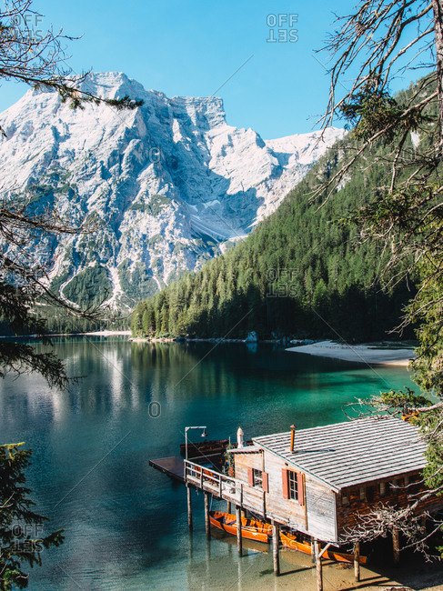 Majestic scenery of wooden house located on shore of clear lake with turquoise water and boats floating on smooth surface on background of mountains in morning light