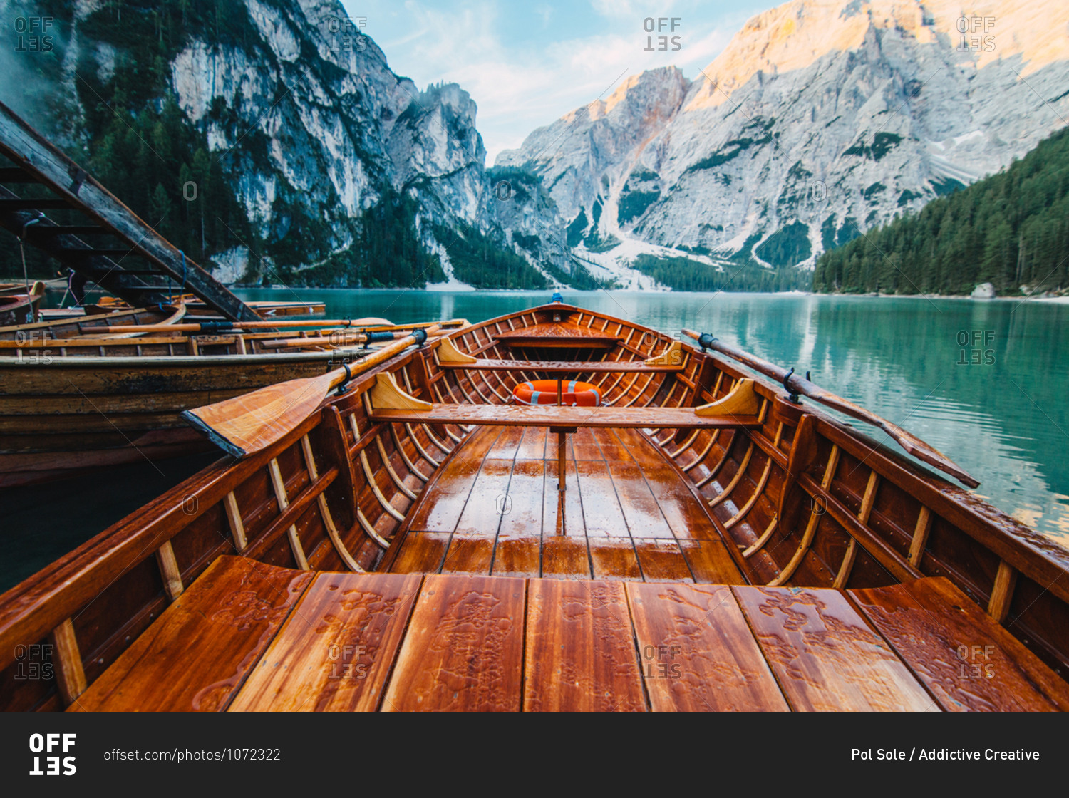 Wooden boat with paddles floating on turquoise water of calm lake on background of majestic landscape of highlands