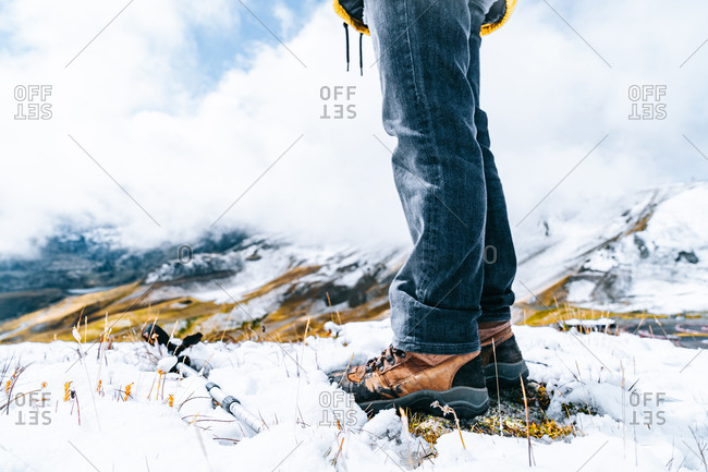 Low angle of legs of crop hiker in warm clothes standing on snowy slope in Pyrenees mountains on sunny day in Andorra