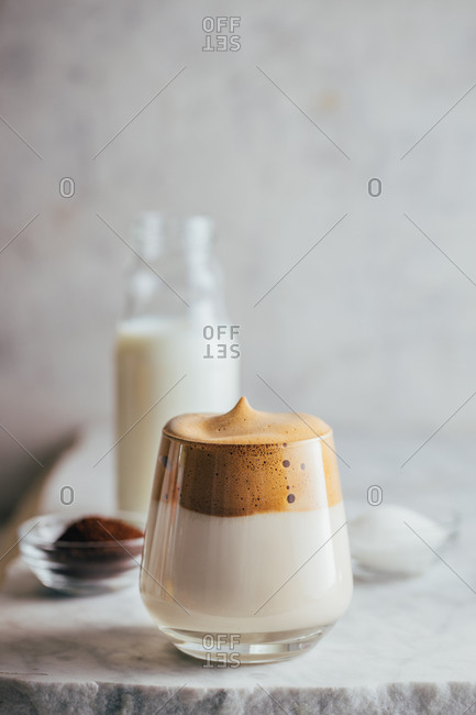 Aromatic Dalgona beverage in glass placed on marble table with bottle of milk, instant coffee and beans