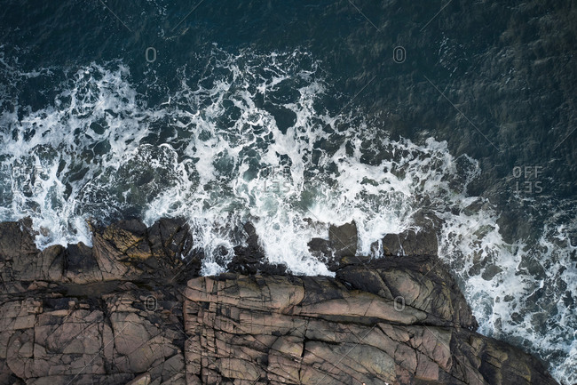 Drone view of foamy blue sea waving on rocky shoreline with rough boulders