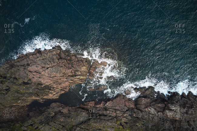 Drone view of foamy blue sea waving on rocky shoreline with rough boulders