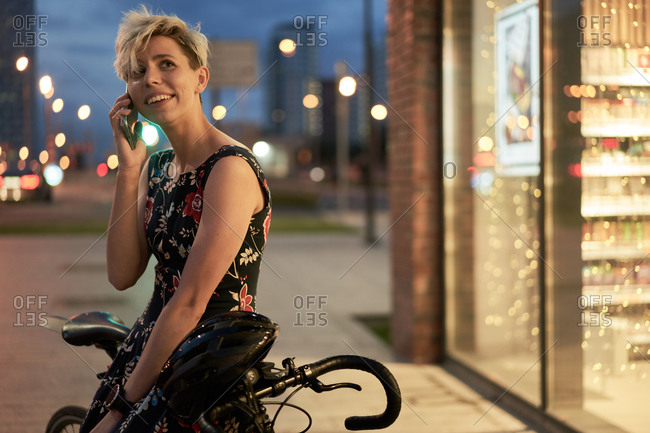 Young woman talking on phone near store and bike at night city