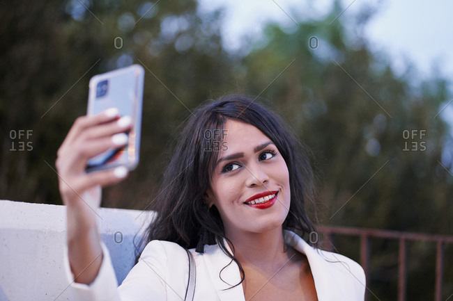 Delighted charming female with red lips standing in evening on street and taking selfie on smartphone