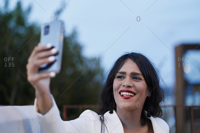 Delighted charming female with red lips standing in evening on street and taking selfie on smartphone