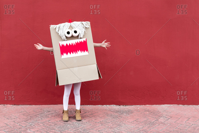 Unrecognizable playful kid wearing funny costume of monster made of carton box standing on street during holiday celebration