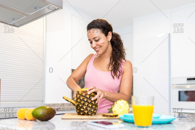 Female cutting ripe pineapple at kitchen counter with fresh fruits while preparing healthy vitamin breakfast at home