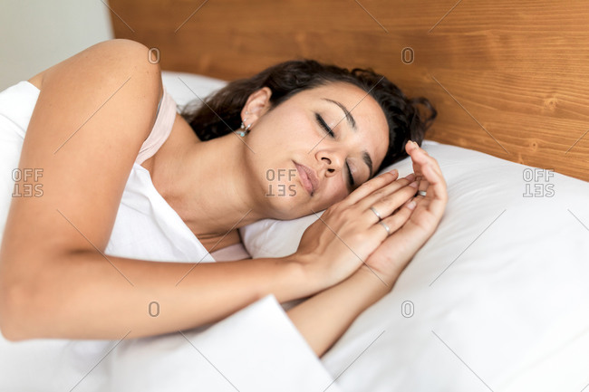 Calm female in pajama lying in bed on soft pillow under white blanket and sweetly sleeping