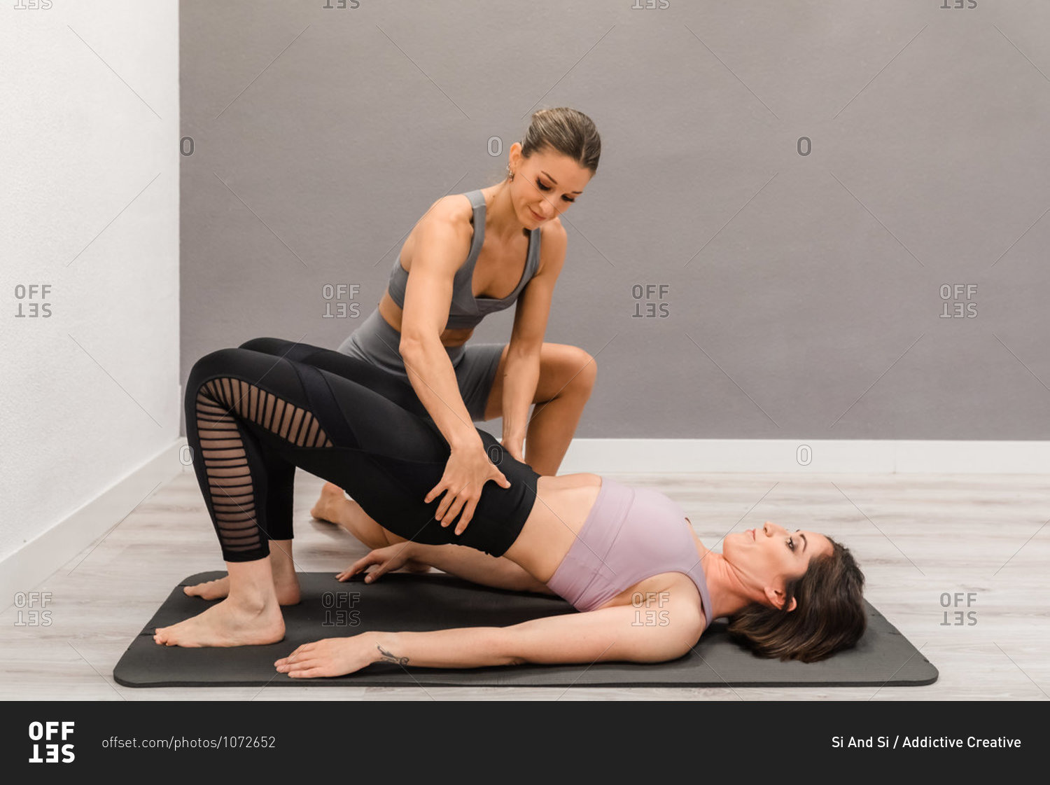 Flexible female lying on mat in Bridge pose and doing yoga with help of professional instructor during class in studio