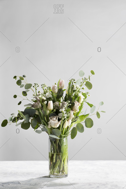Floral arrangement in glass vase with roses and eucalyptus on a textured background with copy space