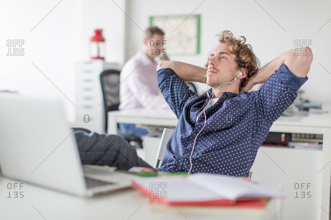 Young office worker reclining at desk with hands behind head