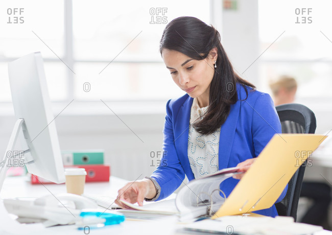 Mid adult businesswoman at looking at file on desk in office