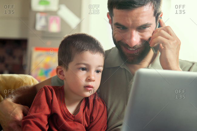 Father on cell phone with son looking at laptop