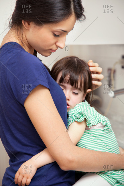 Mother holding tired daughter in the kitchen