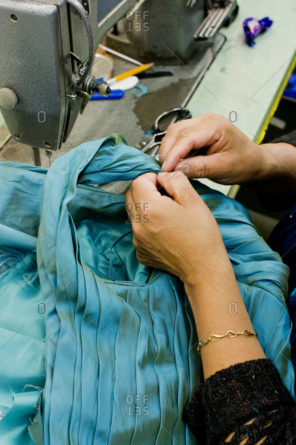 Hands of seamstress sewing turquoise evening gown in design studio