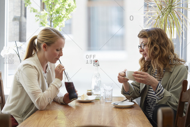 Two female friends drinking and chatting in cafe