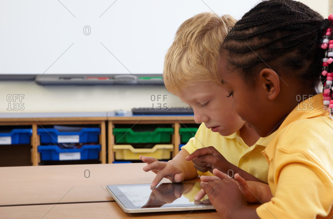 Two school children using computer notebook in classroom