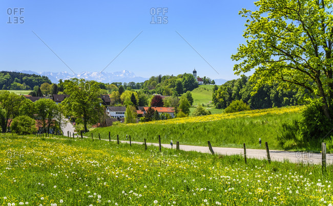 Germany, bavaria, upper bavaria, tiler land, munsing, holzhausen district, spring landscape and town view with parish church of st. johann baptist against wetterstein mountains with zugspitze
